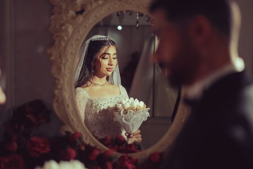 Free Elegant bride holding flowers, reflected in a decorative mirror, creating a serene wedding moment. Stock Photo