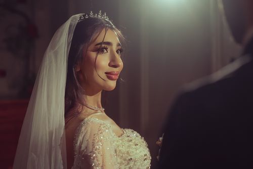Free Bride in a sparkling gown smiling during a wedding ceremony, lit by warm ambient light. Stock Photo
