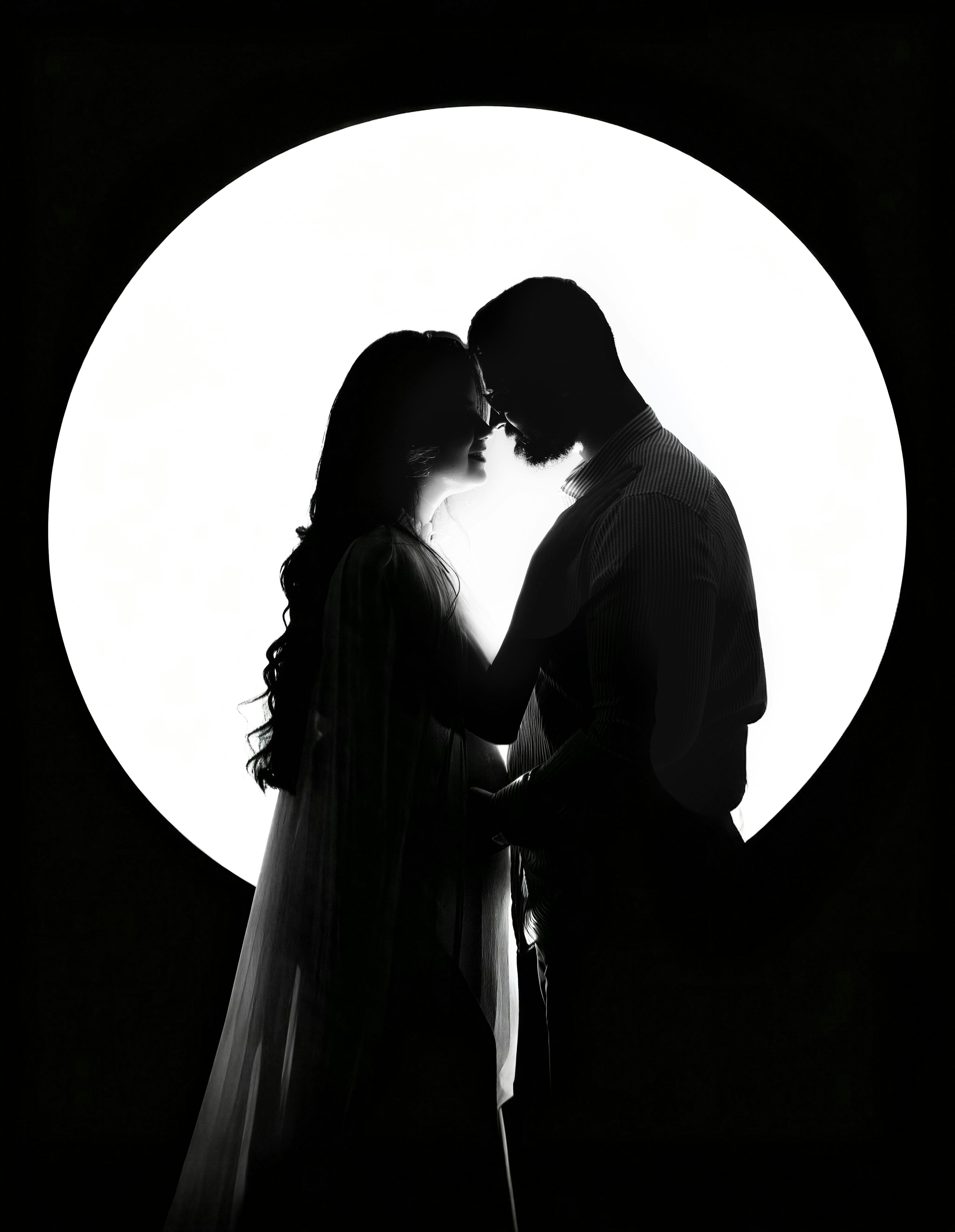 Silhouette of a couple embracing in front of a circular light backdrop.