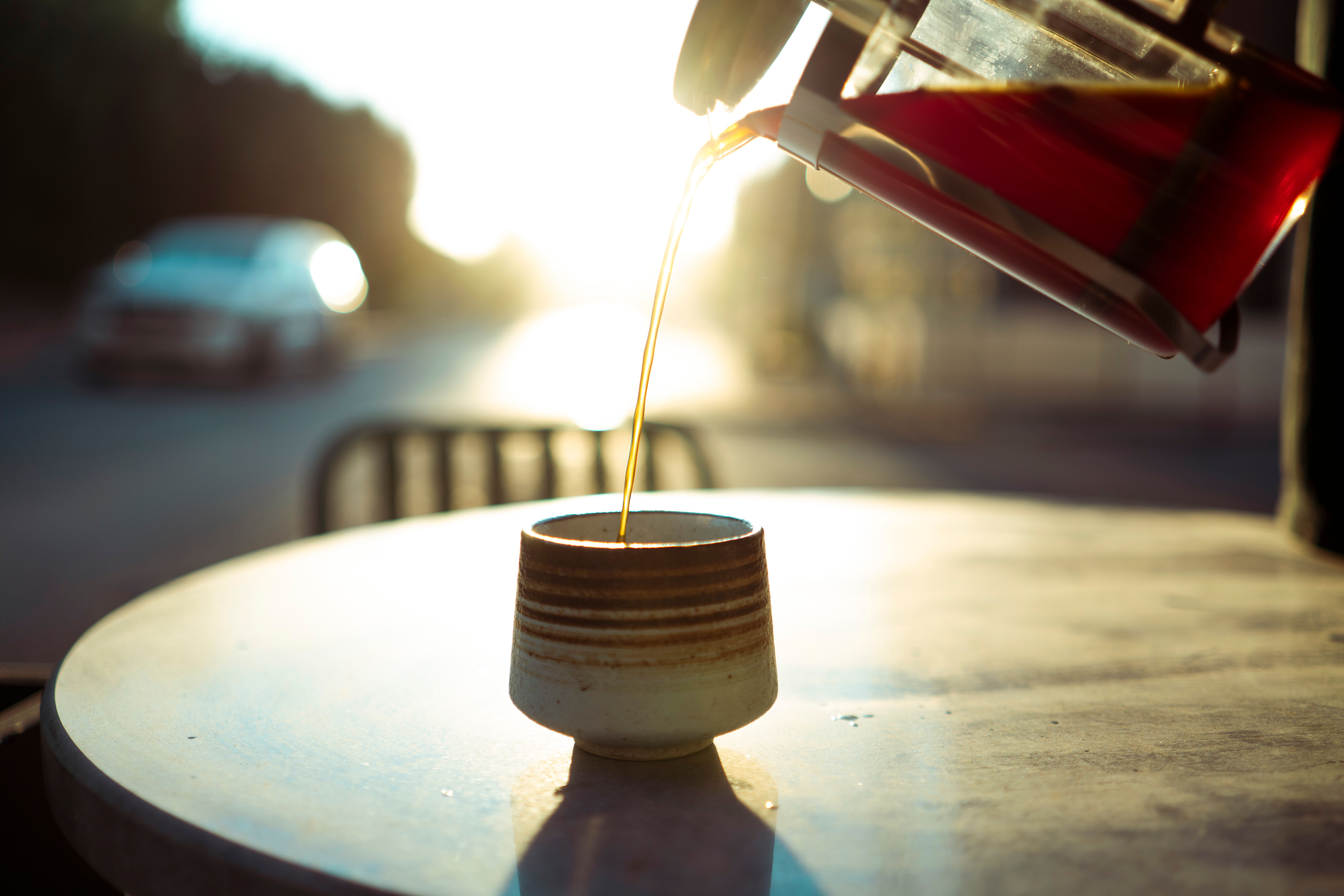 person in morning sunlight at a breakfast table with a glass of water and supplement capsule in hand, fresh fruit visible on the plate