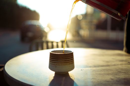 Warm sunlight catches a fresh cup of coffee being poured outdoors on a Baghdad street.