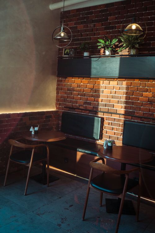 Free Warm sunlight casts on a stylish cafe corner with exposed brick, plants, and modern chairs. Stock Photo