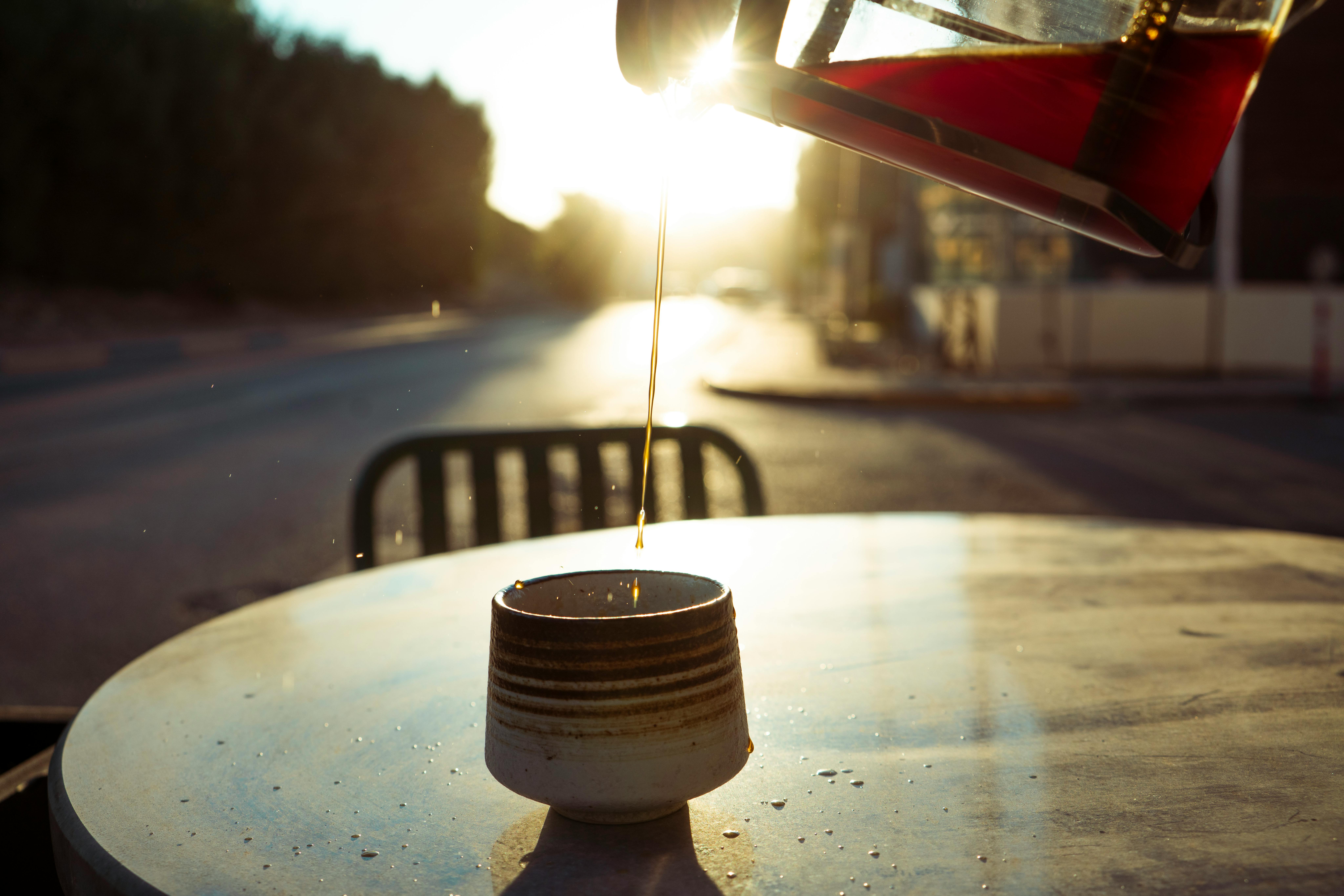 Sunlit coffee being poured into a cup on a Baghdad street table, capturing morning light.