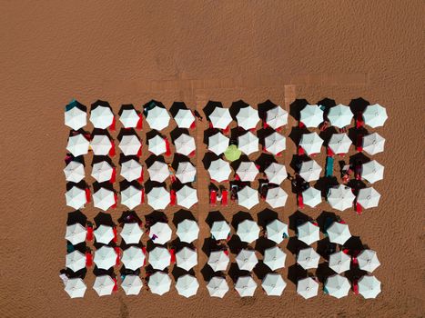 Aerial shot of white beach umbrellas arranged on a sandy beach in Greece, offering a symmetrical view.
