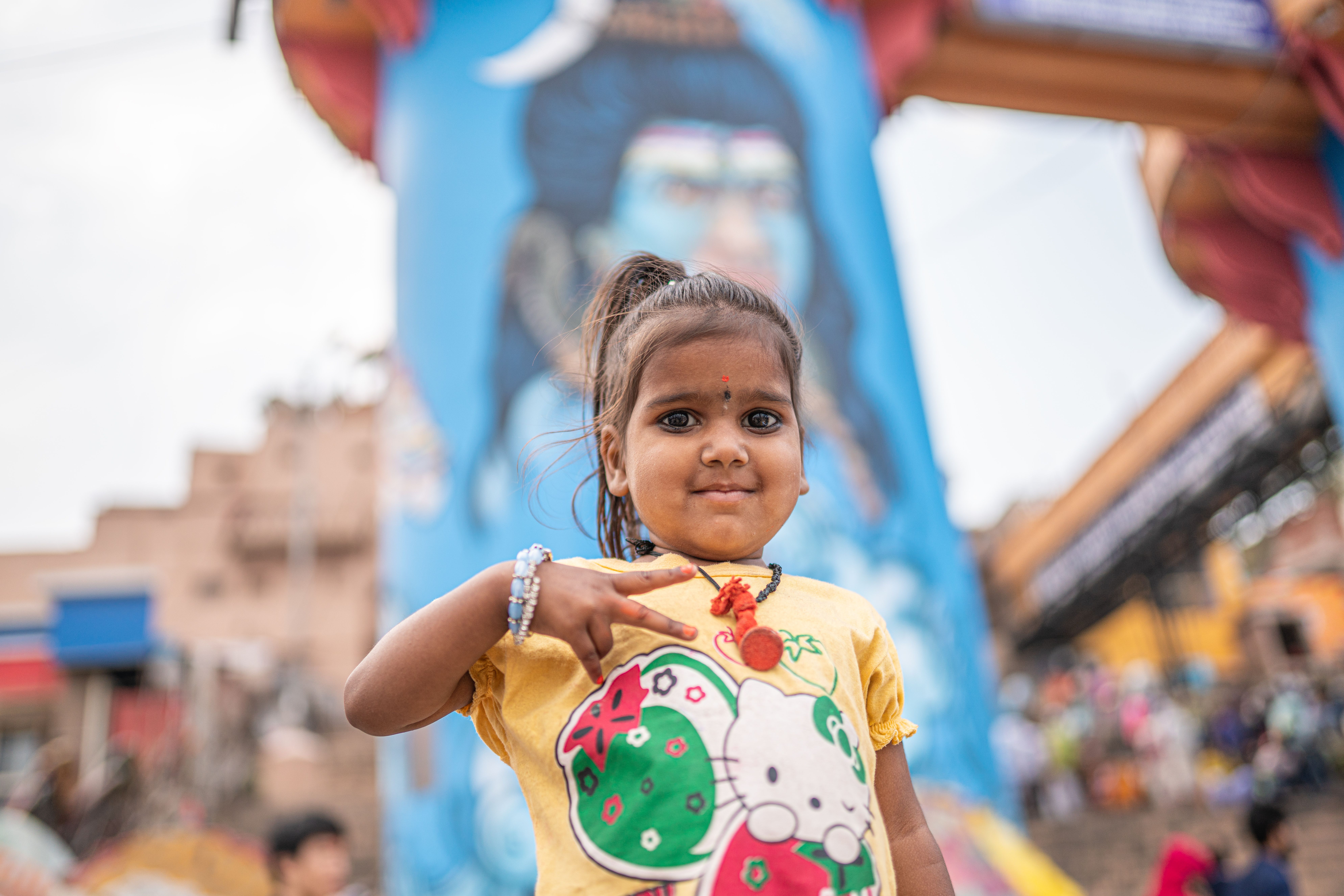 A young girl poses in front of a vibrant Shiva mural in Varanasi, capturing local culture and spirit.