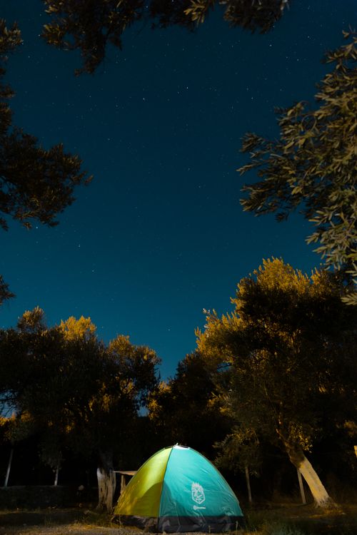 Free A serene camping scene with a tent under a starry night sky surrounded by trees. Stock Photo