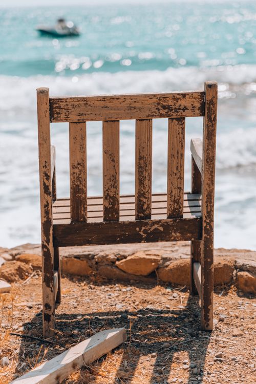 Free Vintage wooden chair facing the ocean on a sunny beach, embodying tranquility and solitude. Stock Photo