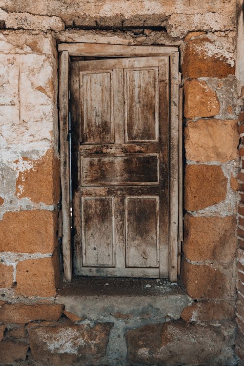 Free A rustic, weathered wooden door set in an old stone wall with warm earthy tones. Stock Photo