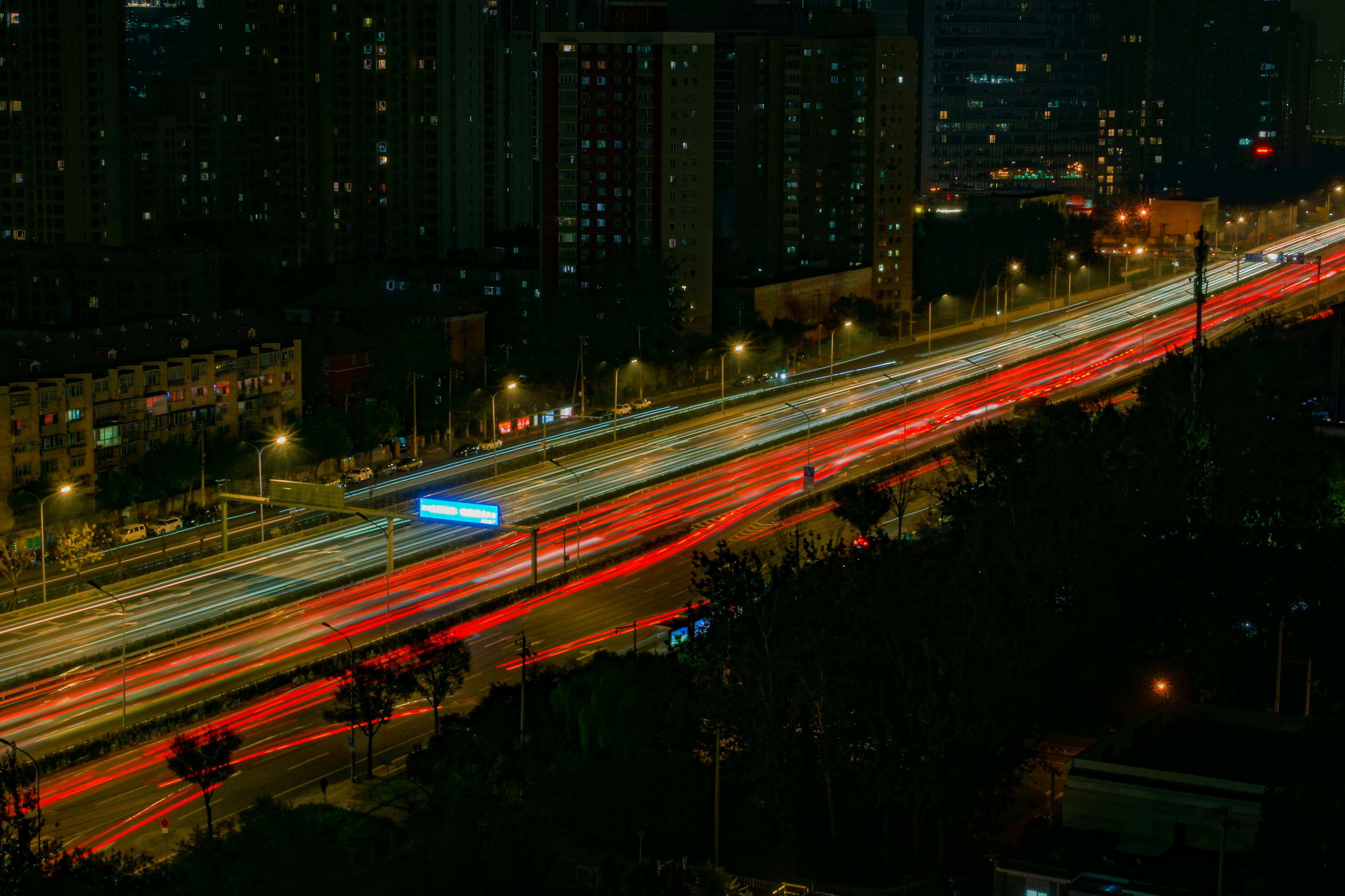 Nighttime view of a busy highway in Beijing with long exposure capturing vibrant light trails of passing vehicles.