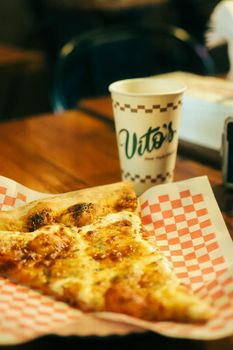 A mouthwatering slice of pepperoni pizza on a checkered paper with a Vito's cup in the background.