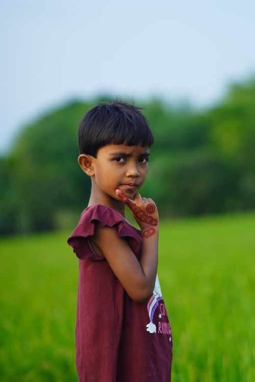 Free A young Bangladeshi girl stands thoughtfully in a lush green field, wearing decorative mehndi on her hand. Stock Photo