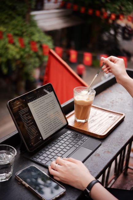 A person working on a tablet at an outdoor cafe table with a latte.