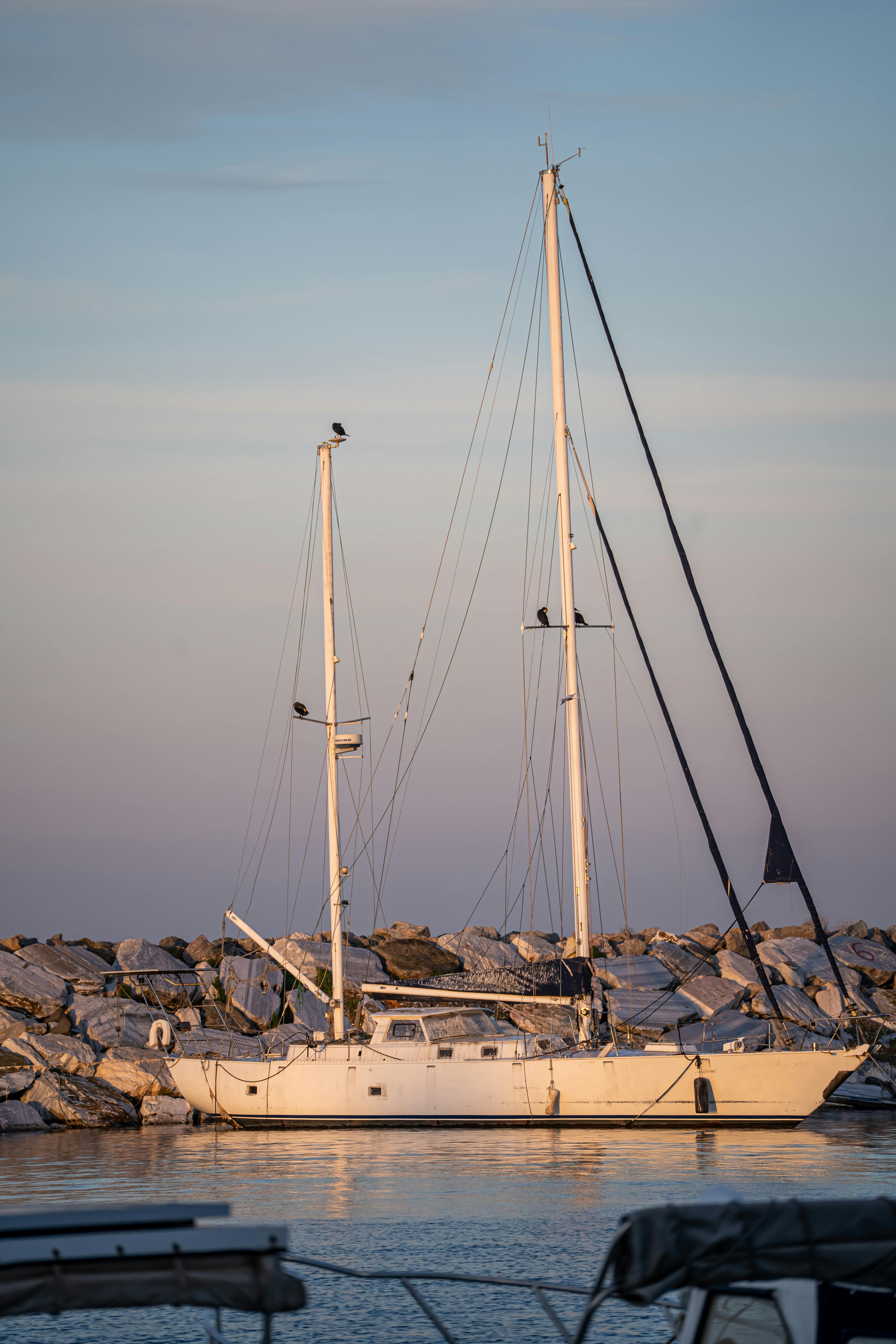 Sailboat docked by a rocky marina at sunset, serene ocean view.