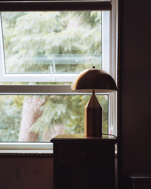 Free Warm interior view featuring a table lamp beside an open window overlooking greenery. Stock Photo