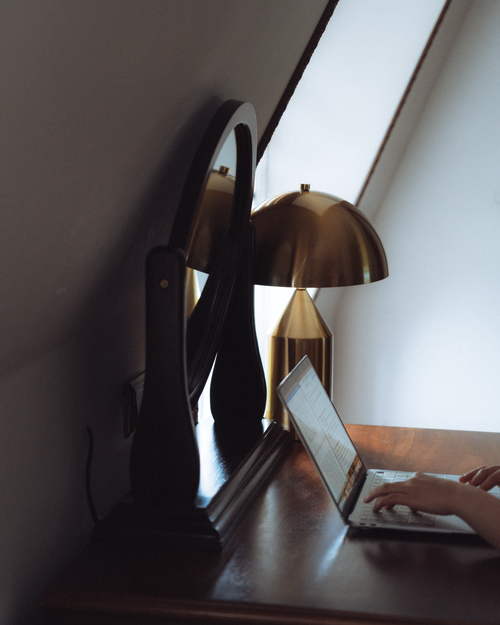Free Quiet workspace with a laptop, gold lamp, and mirror on a wooden desk, creating a cozy atmosphere. Stock Photo