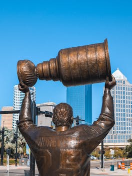 Bronze statue of a hockey player lifting the Stanley Cup in Tampa's urban landscape.