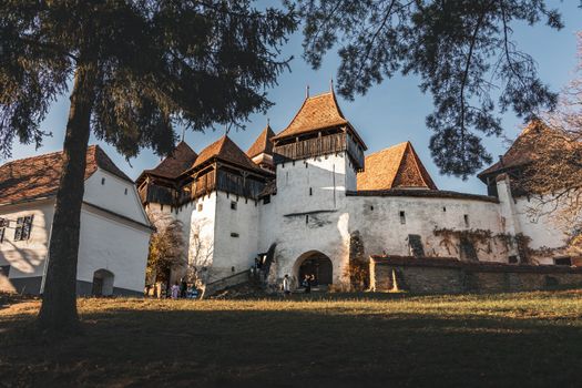 Historic fortified church surrounded by rural landscape at sunset in Romania, showcasing traditional architecture.