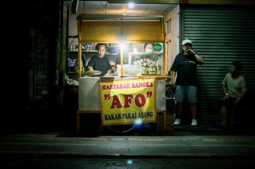 Free A vibrant street food vendor stall by night, serving Martabak Bangka 'AFO' in a bustling market scene. Stock Photo