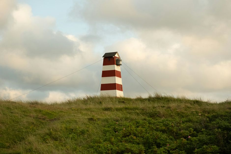 Scenic lighthouse on a grassy hill in Thisted, Denmark under a cloudy sky.