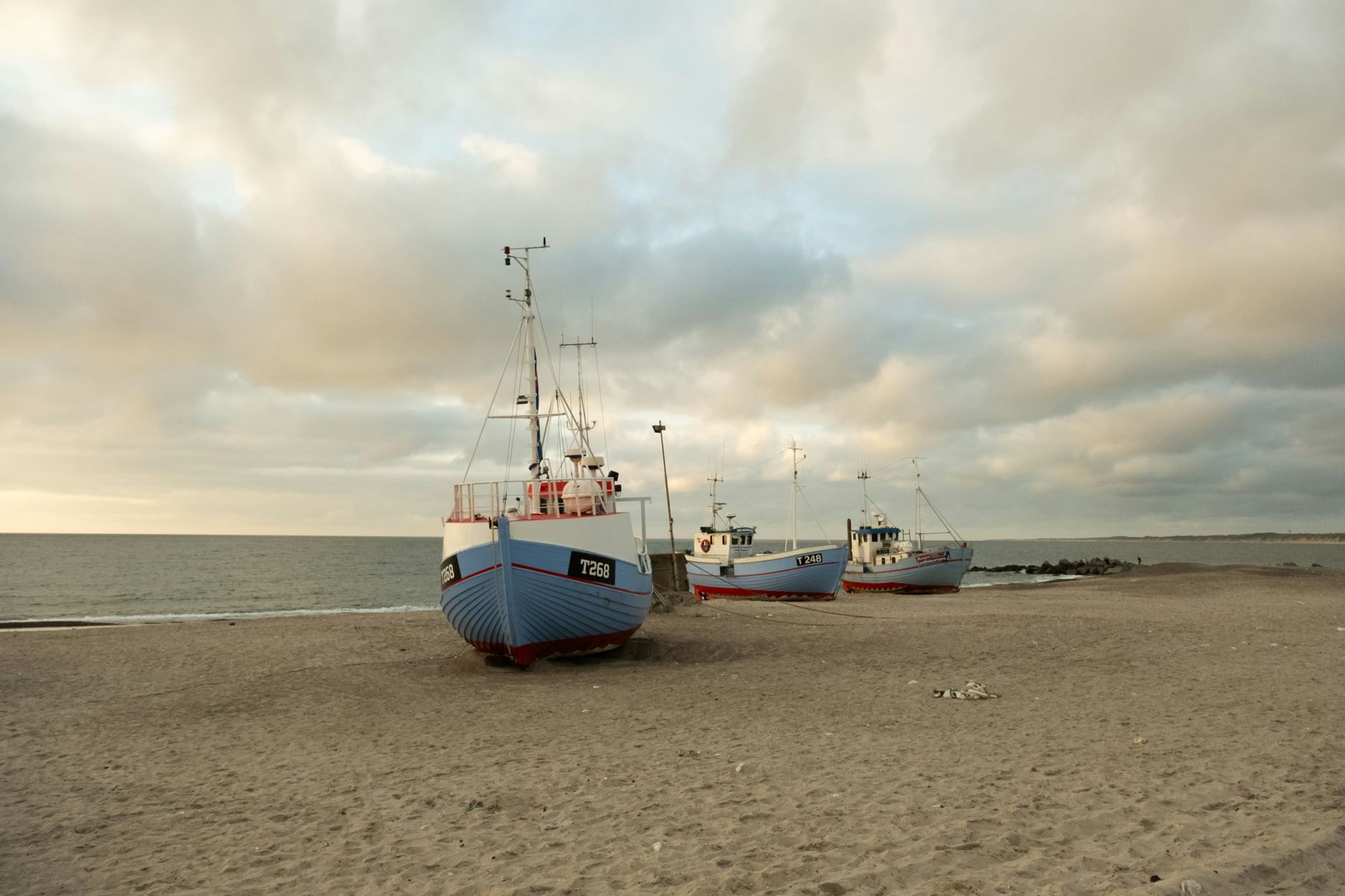 Fishing boats anchored on the sandy shores of Thisted, Denmark during a calm sunset.