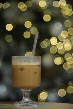 A refreshing iced coffee in a glass cup against a festive background with warm bokeh lights.