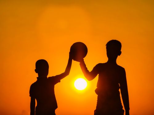 Free Silhouette of two children holding a ball against a vivid sunset sky, symbolizing friendship and play. Stock Photo