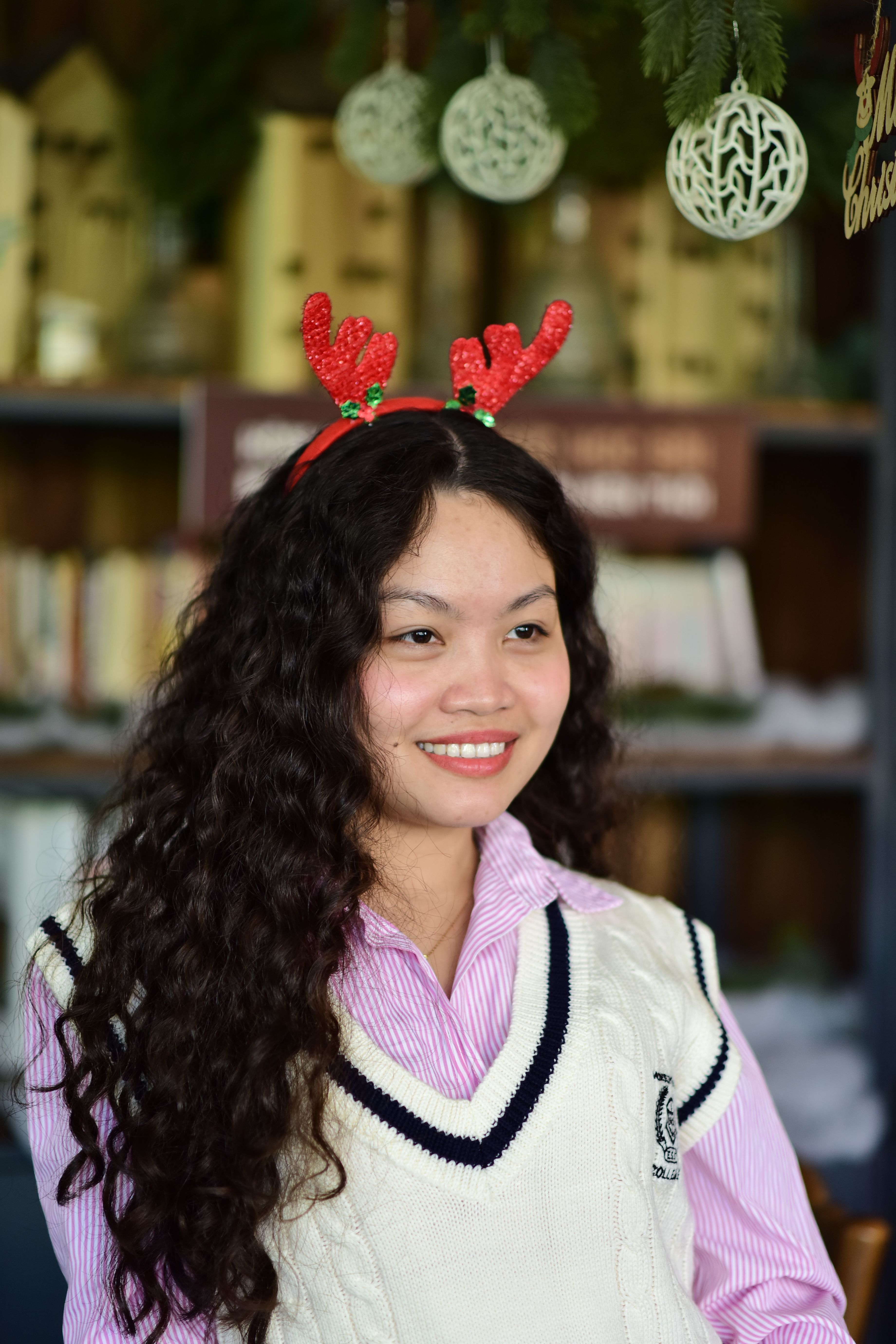 Cheerful woman wearing red reindeer antler headband indoors, smiling.