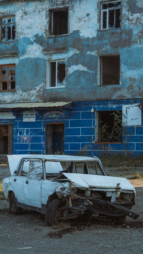 Free A rusty, abandoned car sits in front of a neglected building, illustrating urban decay. Stock Photo