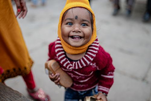 Free A joyful baby wearing warm clothing smiles cheerfully on a street in Varanasi, India. Stock Photo