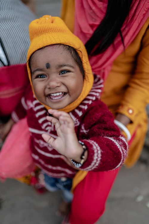 Free Smiling child in a bright knit sweater and hat enjoying a day outdoors in Varanasi, India. Stock Photo