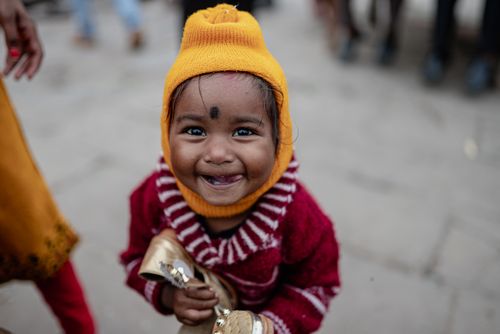 Free A happy child in a colorful winter outfit smiles brightly in the streets of Varanasi. Stock Photo