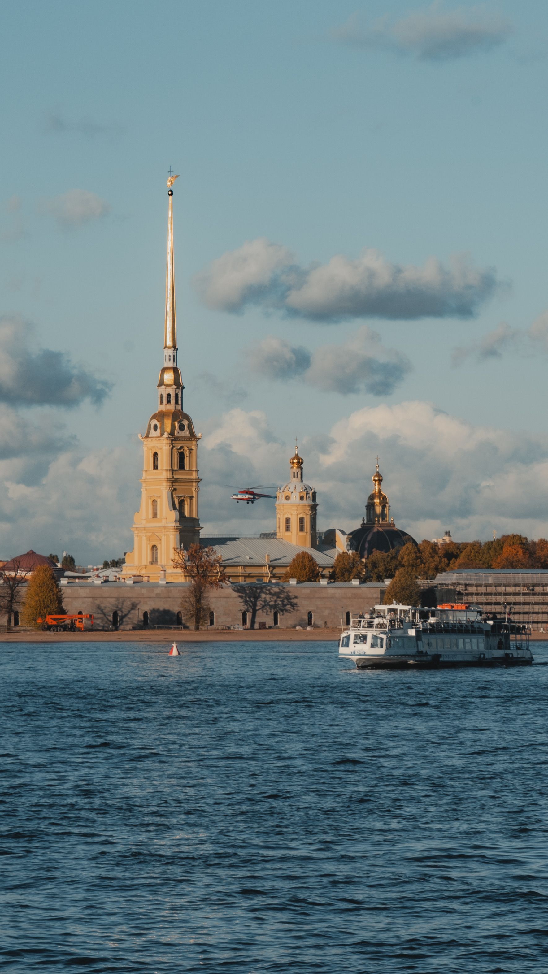 Serene autumn view of the Peter and Paul Fortress with water and boat in foreground.