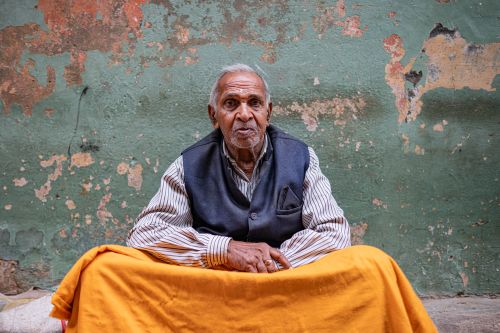 Free Portrait of an elderly man seated against a textured wall in Varanasi, India, exuding wisdom and calmness. Stock Photo