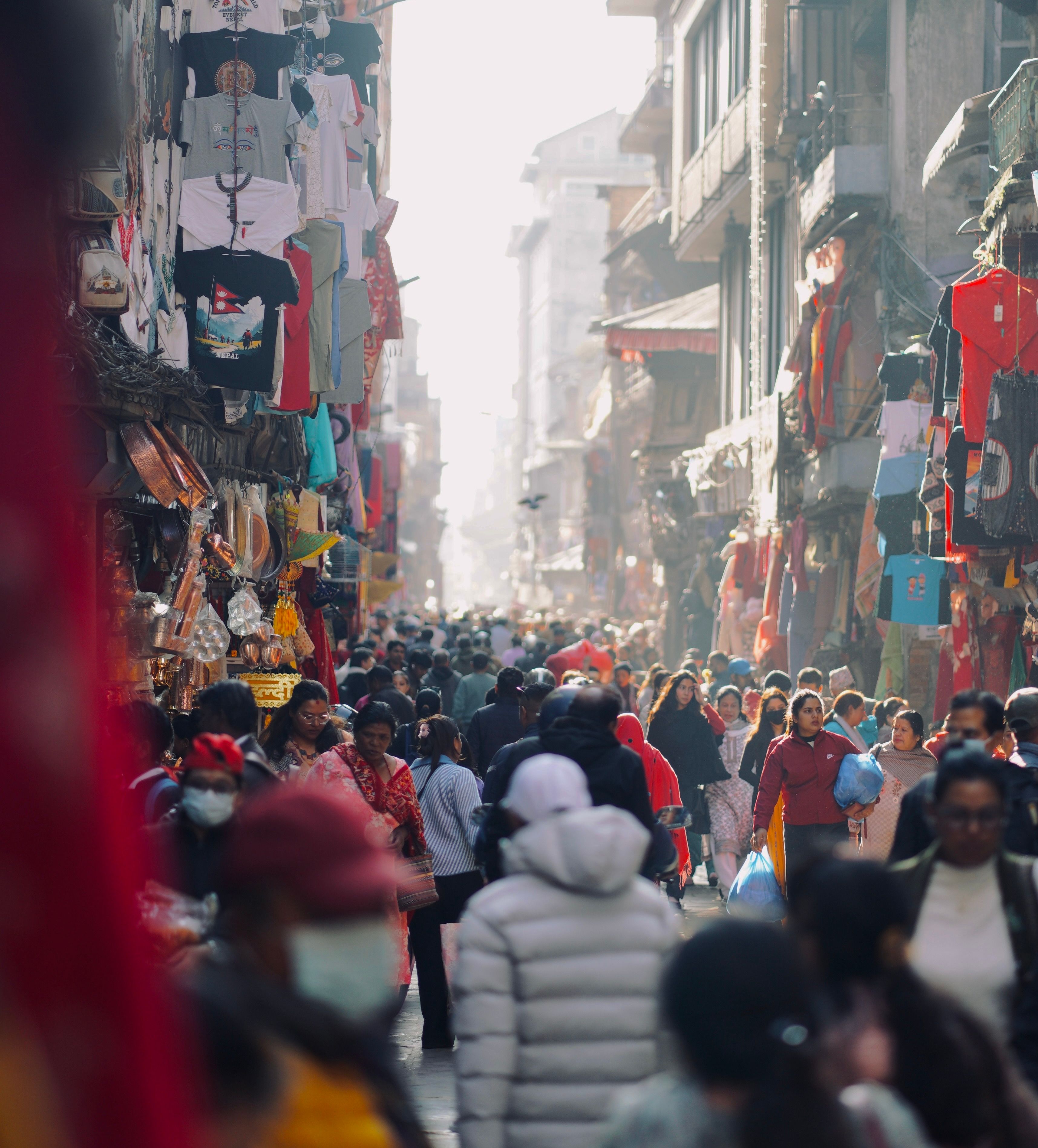 Crowded market street in Bhaktapur, Nepal with people shopping and vibrant textiles displayed.