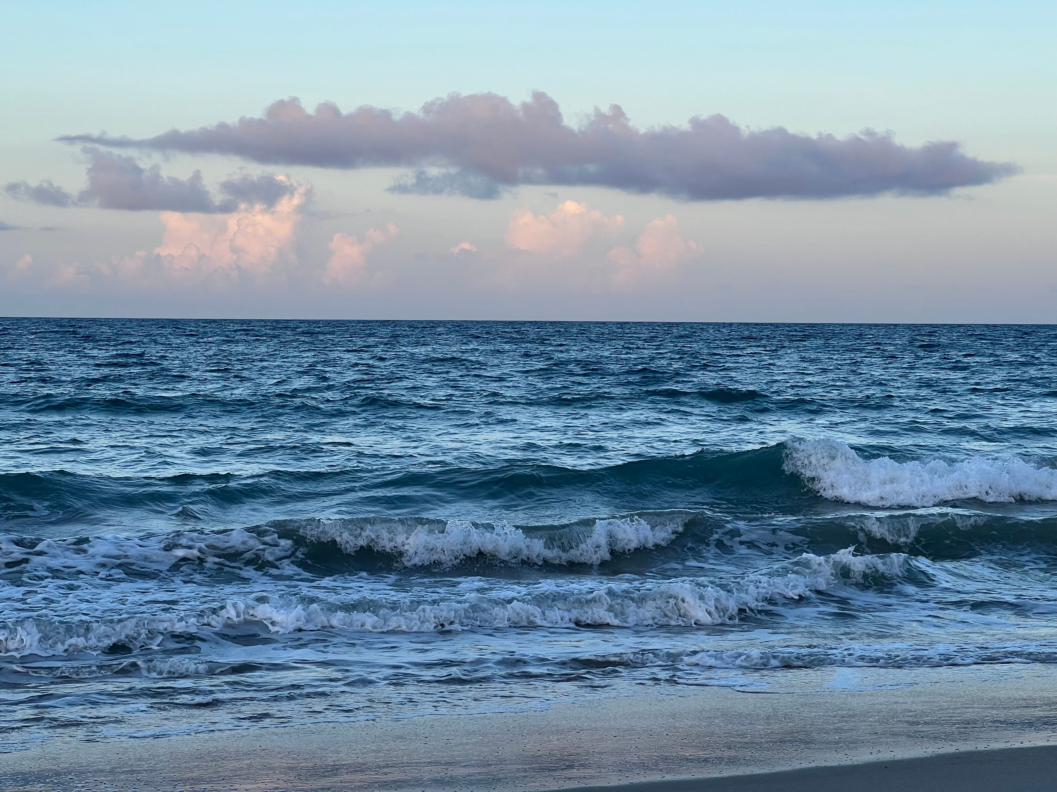 Serene ocean view with gentle waves and a pastel-hued sky at sunrise on a Florida beach.