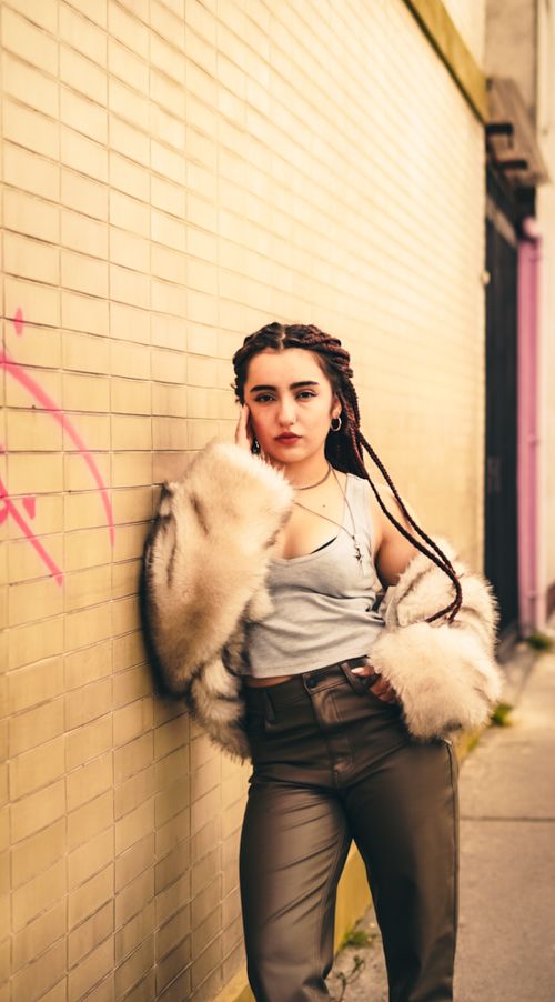 Free Fashionable woman with braids poses against a graffiti-covered urban wall, radiating confidence and style. Stock Photo