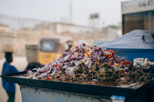 Outdoor street food stall with chopped onions and meat in a bustling city.