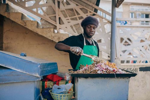 Free Street vendor preparing traditional African dish outdoors, showcasing vibrant culture. Stock Photo