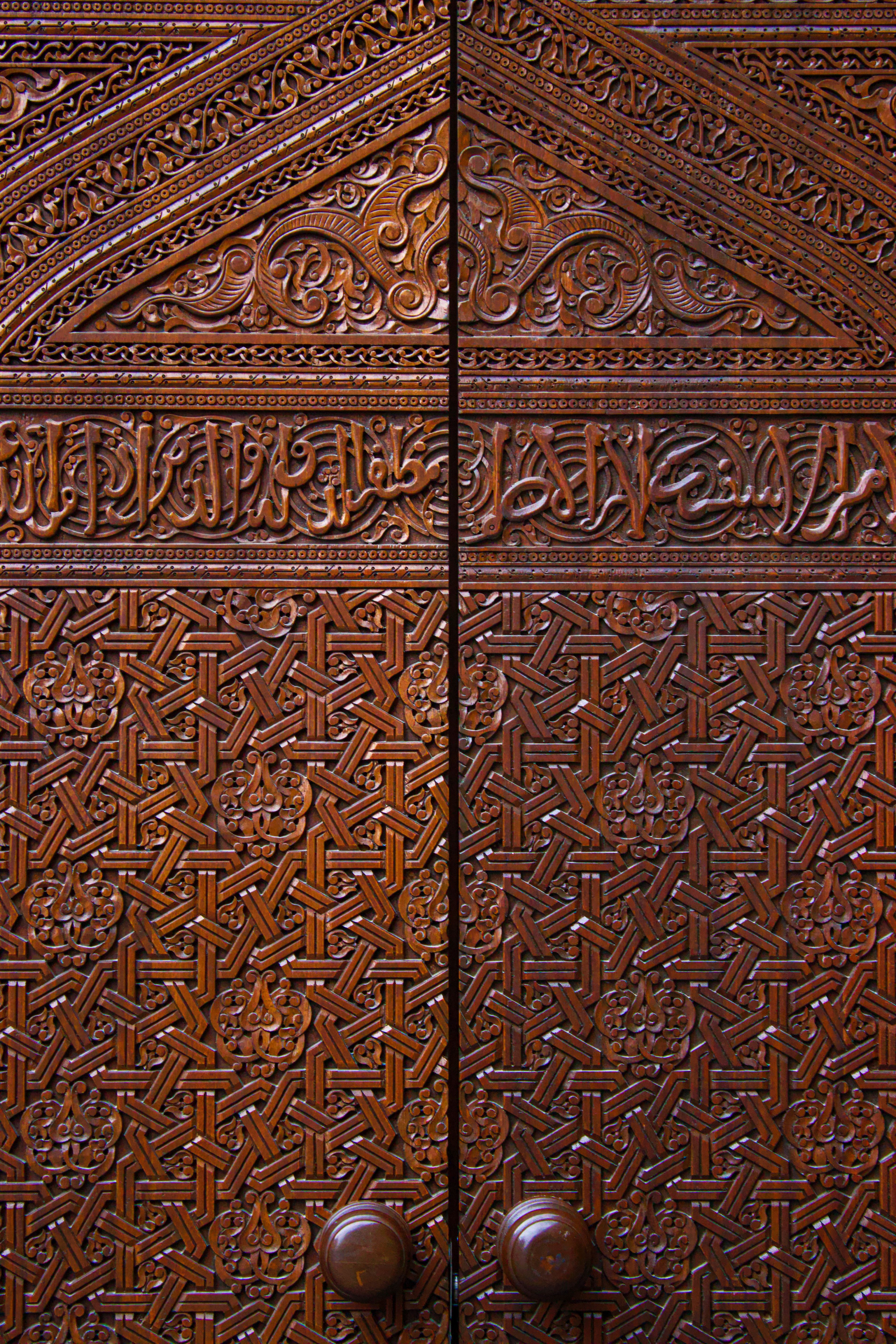 Fotomural Puerta de madera elaboradamente tallada con patrones geométricos y escritura árabe.