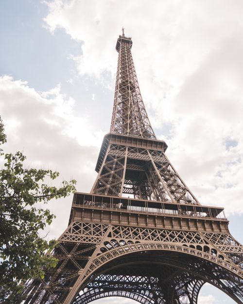 Free Capture of the Eiffel Tower in Paris with a backdrop of cloudy skies and lush greenery. Stock Photo