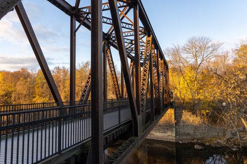 Free Iron bridge crossing with fall foliage in Auburn, Maine during golden hour. Stock Photo