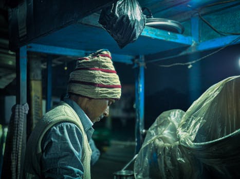A street vendor in winter attire prepares food under dim light during the night.