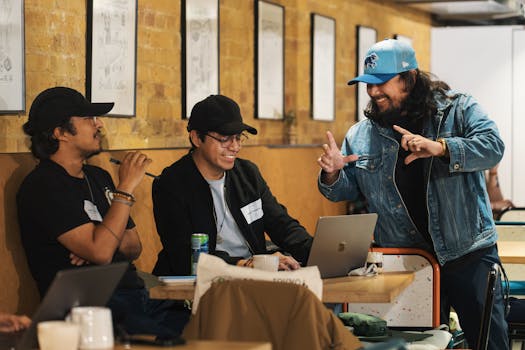 Three people collaborate in a trendy cafe setting, discussing over a laptop.