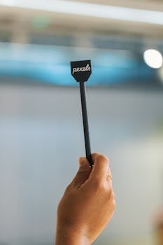 A hand holding a small sign with 'pexels' text, blurred background.