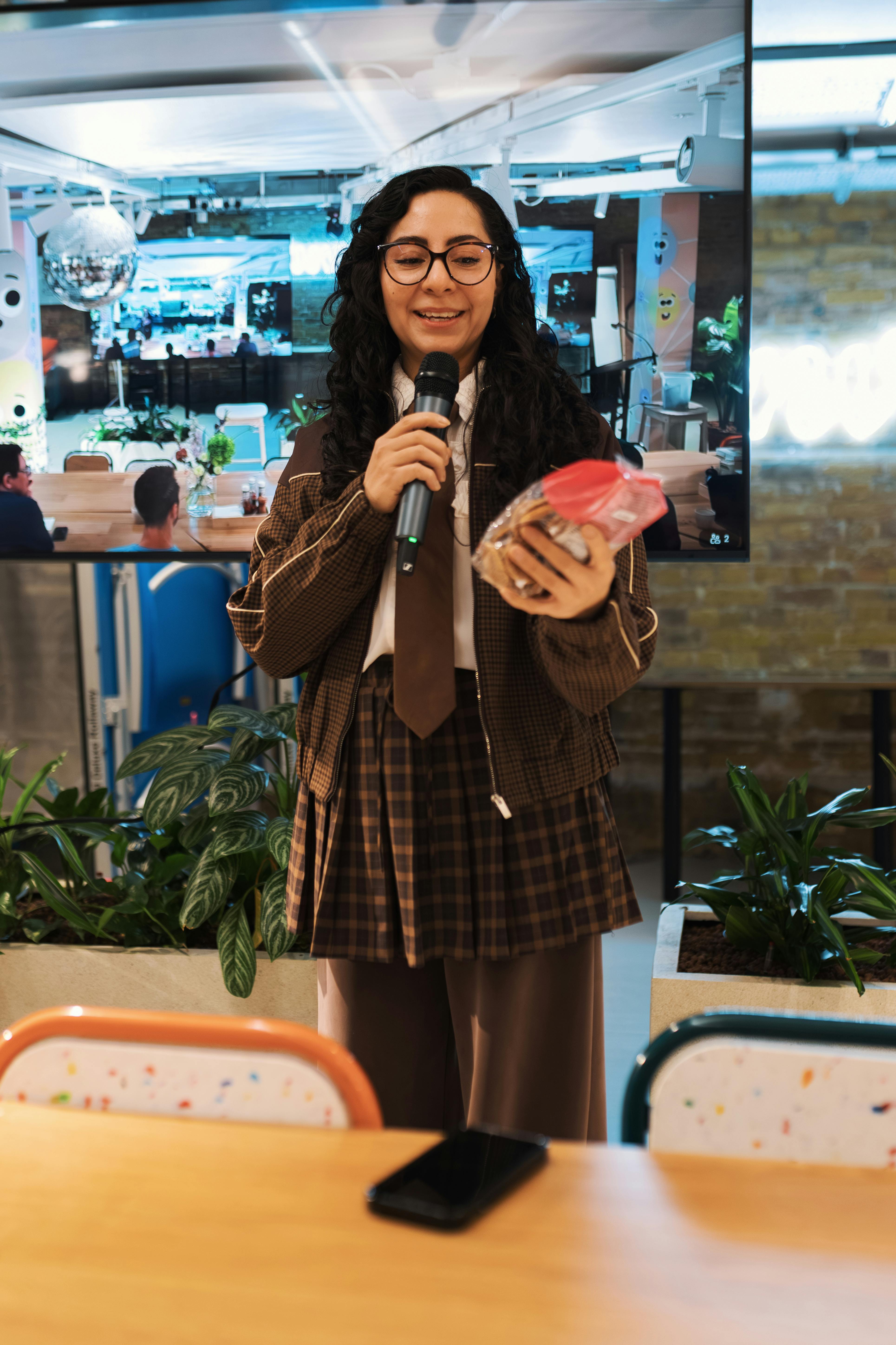 Young woman speaking into microphone holding a gift in a modern office setting.