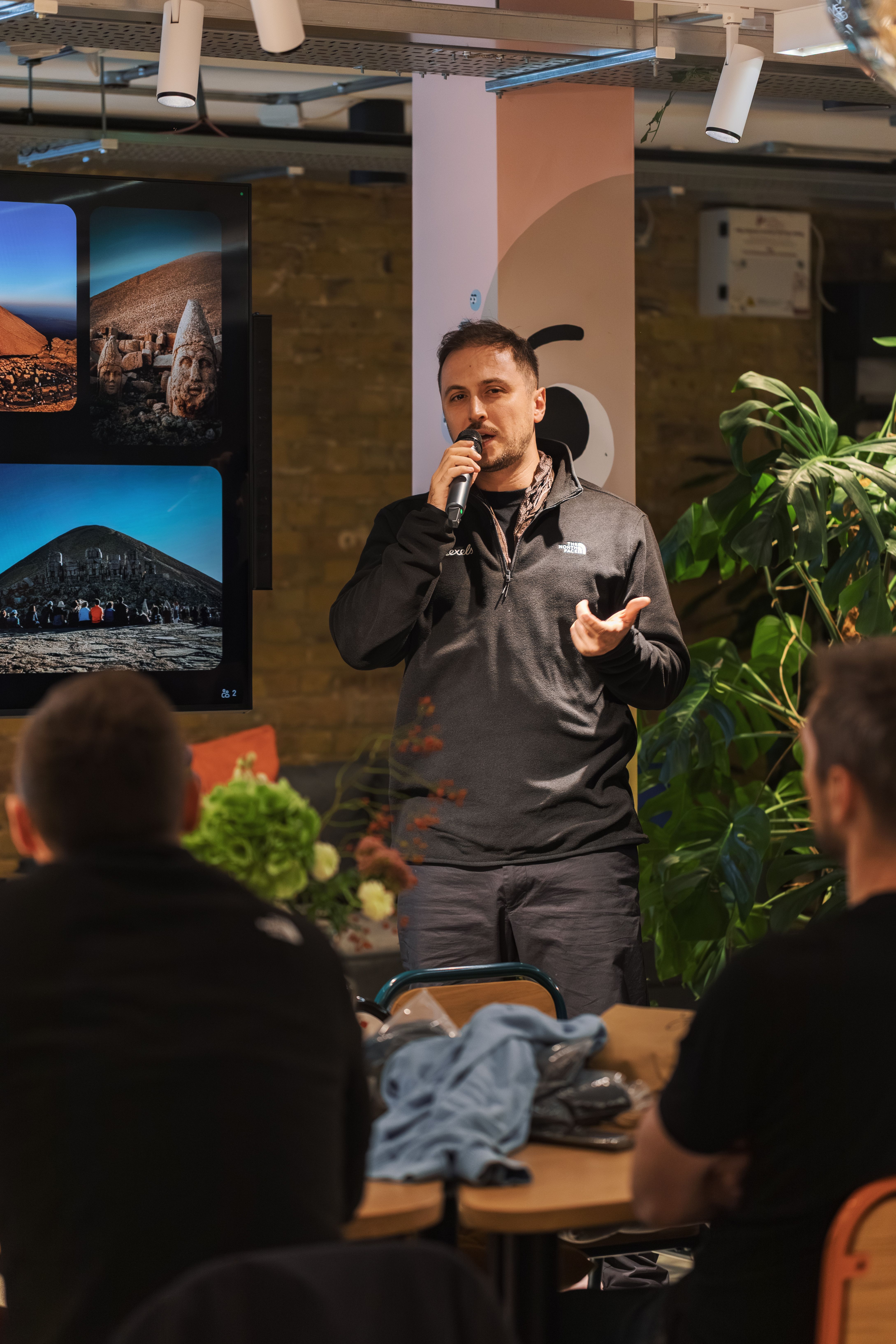 A man presenting to a seated audience with visuals on screen.