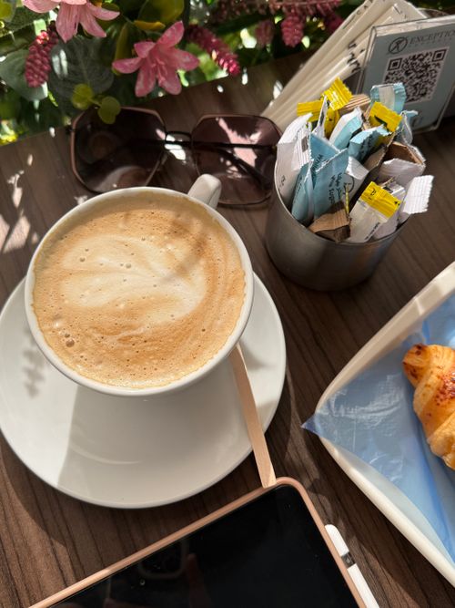 Free Table with coffee, croissant, sunglasses, and flowers in morning light. Stock Photo