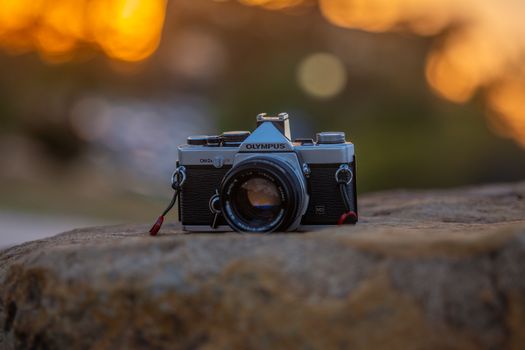 Classic Olympus camera resting on a rock with blurred sunset bokeh.