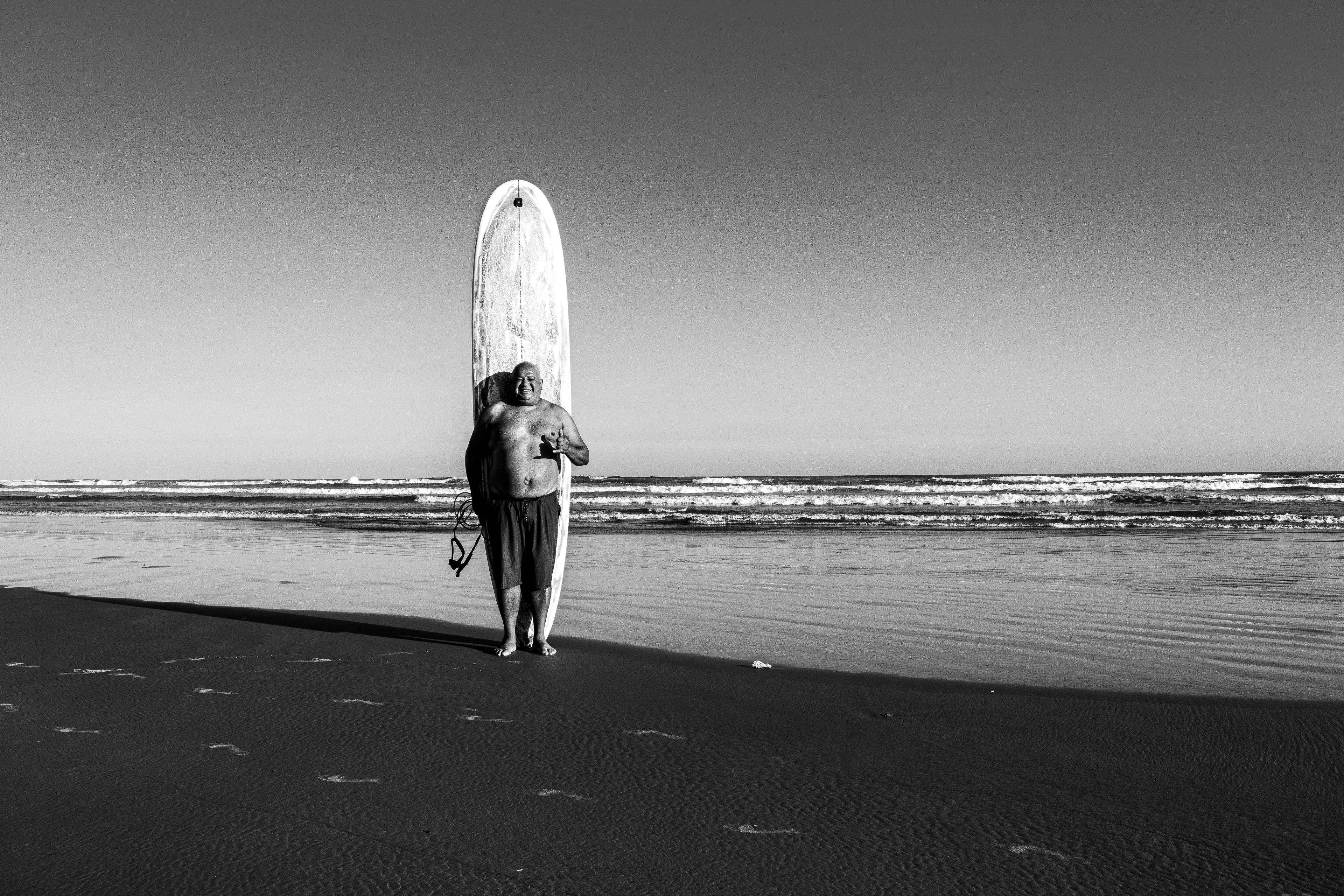 Black and white photo of a man with a surfboard on Praia Grande beach, São Paulo.