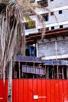 Construction worker on a building site in Praia Grande, São Paulo with red barriers and palm trees.
